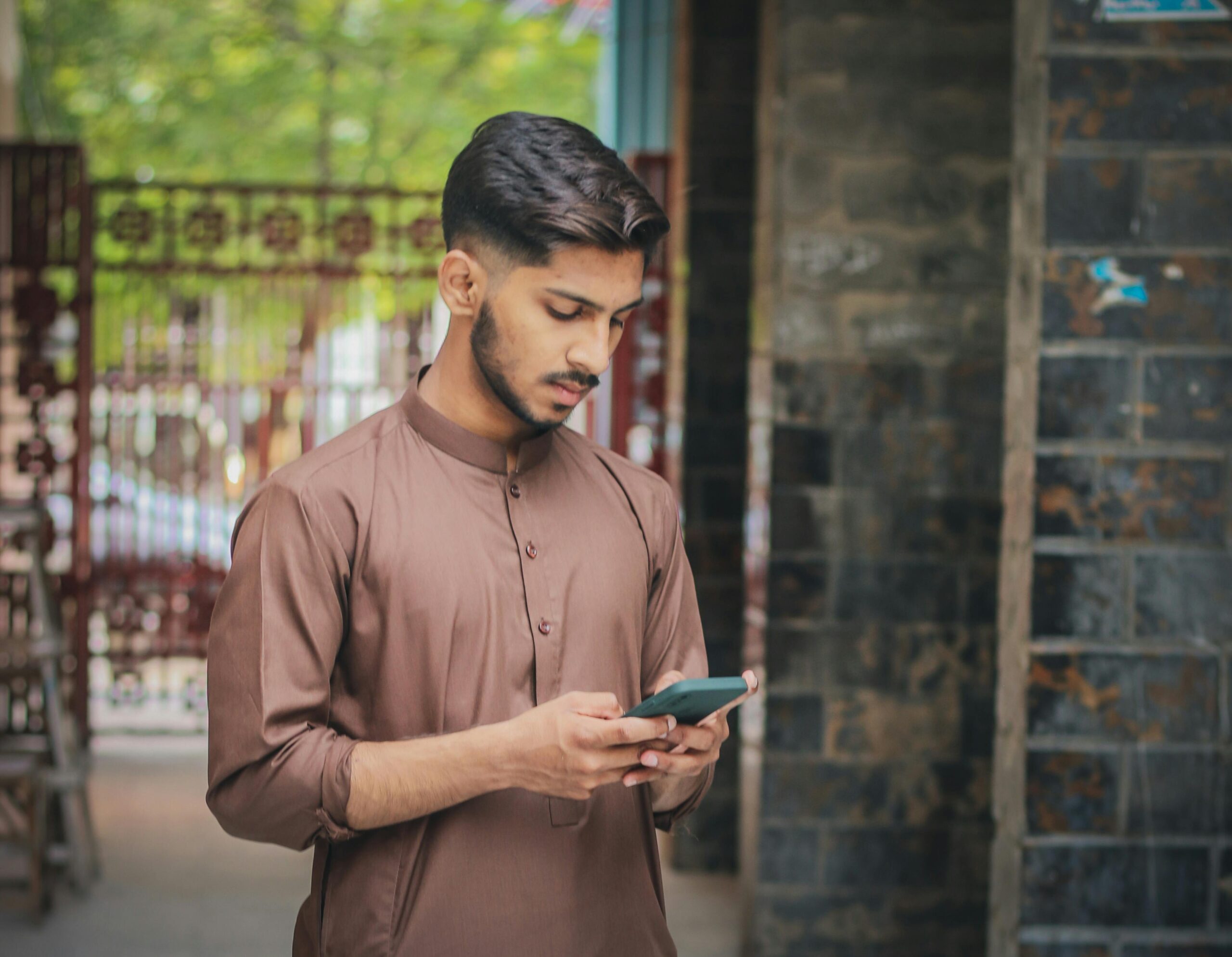 A young man in traditional attire uses his phone while standing outdoors in Pakistan.